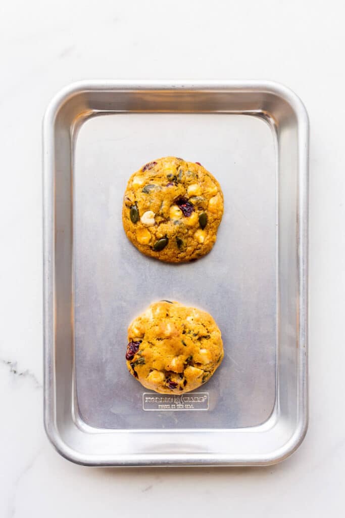 Two cookies on a small baking pan, but one is flatter than the other.