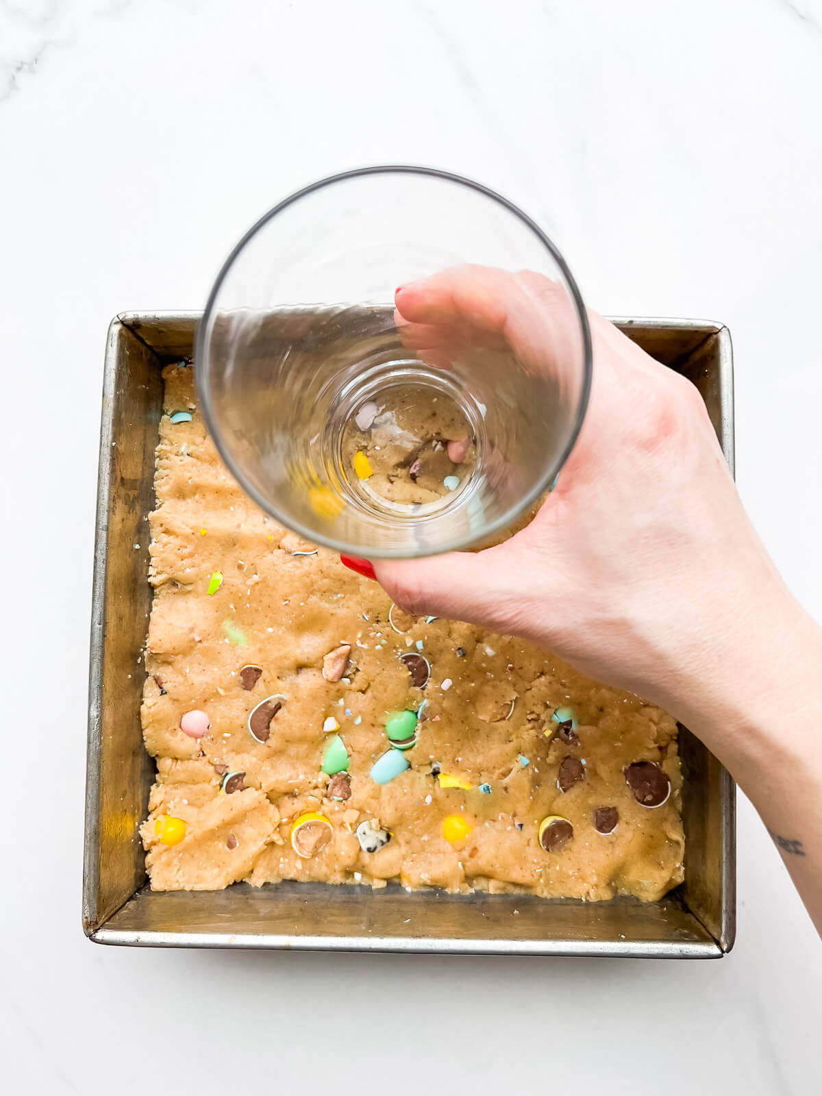 Pressing cookie dough into a brownie pan with a flat-bottomed glass to make blondies.