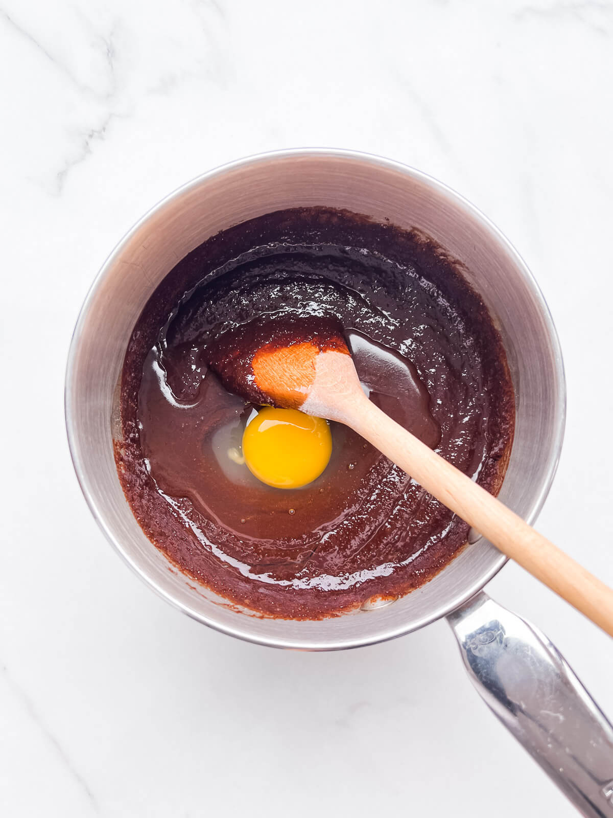 Adding raw eggs to brownie batter with a wooden spoon.