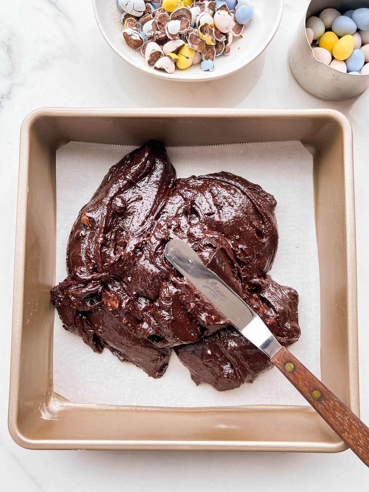 Spreading brownie batter in a metal baking pan with a mini offset spatula.