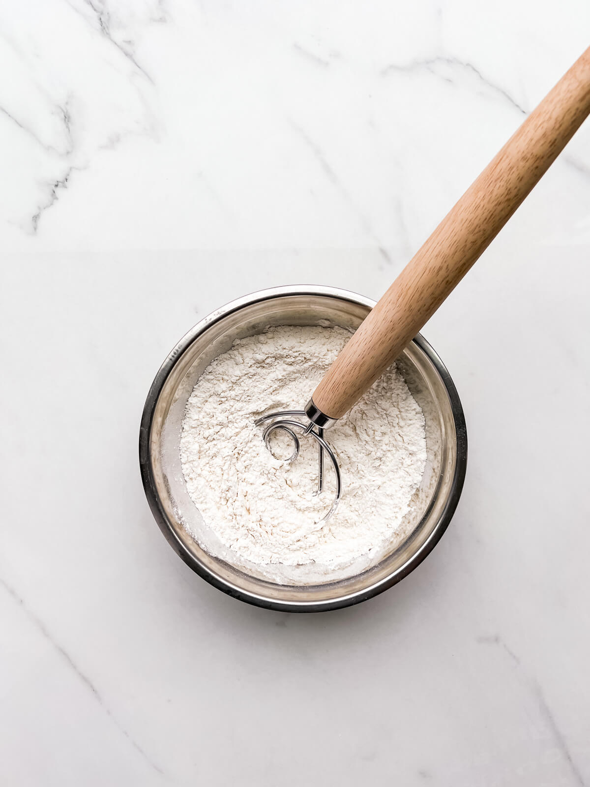 Whisking dry ingredients in a stainless steel bowl with a whisk.