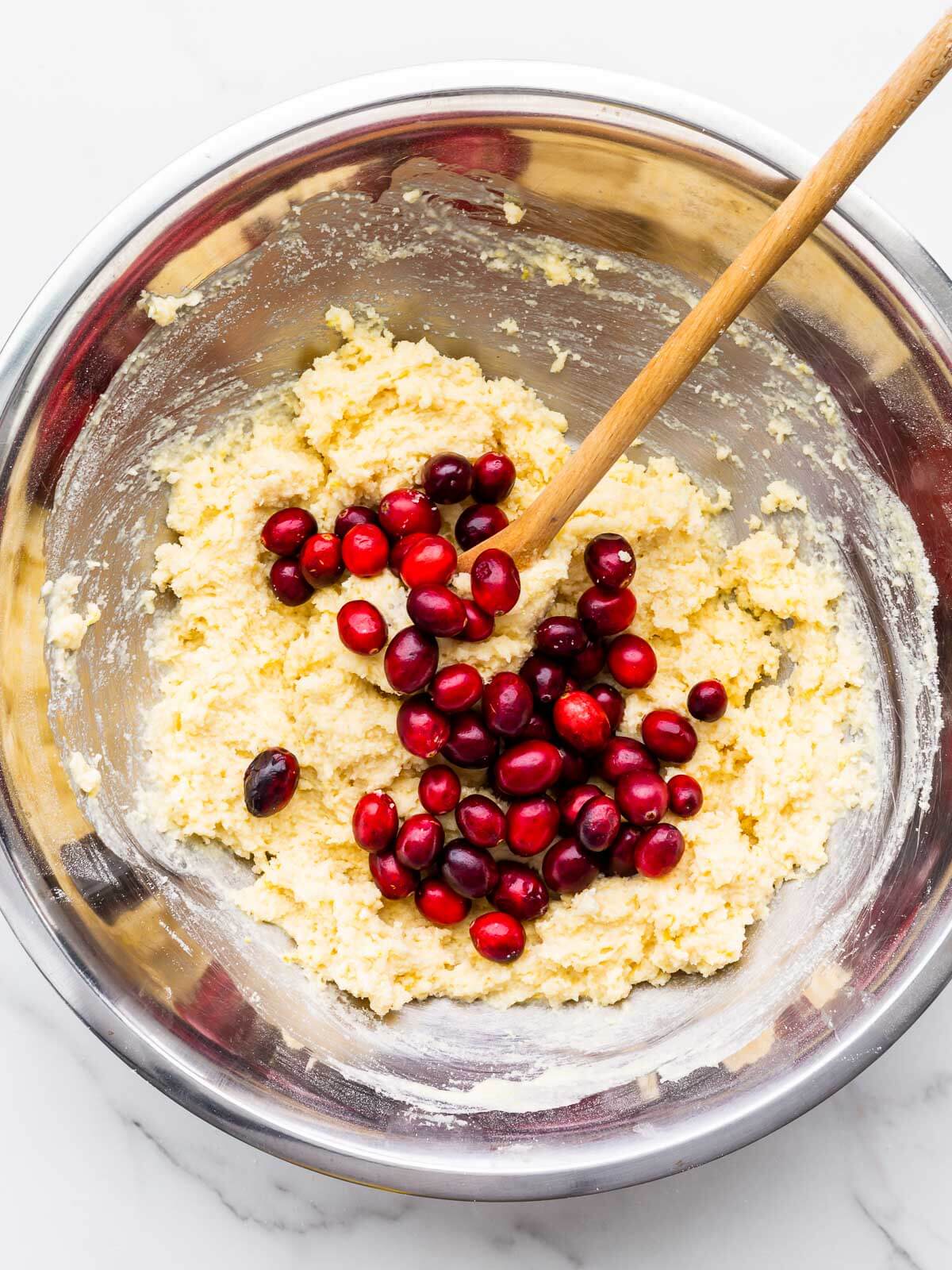 Incorporating fresh cranberries in a bowl of lemon muffin batter before scooping and baking.