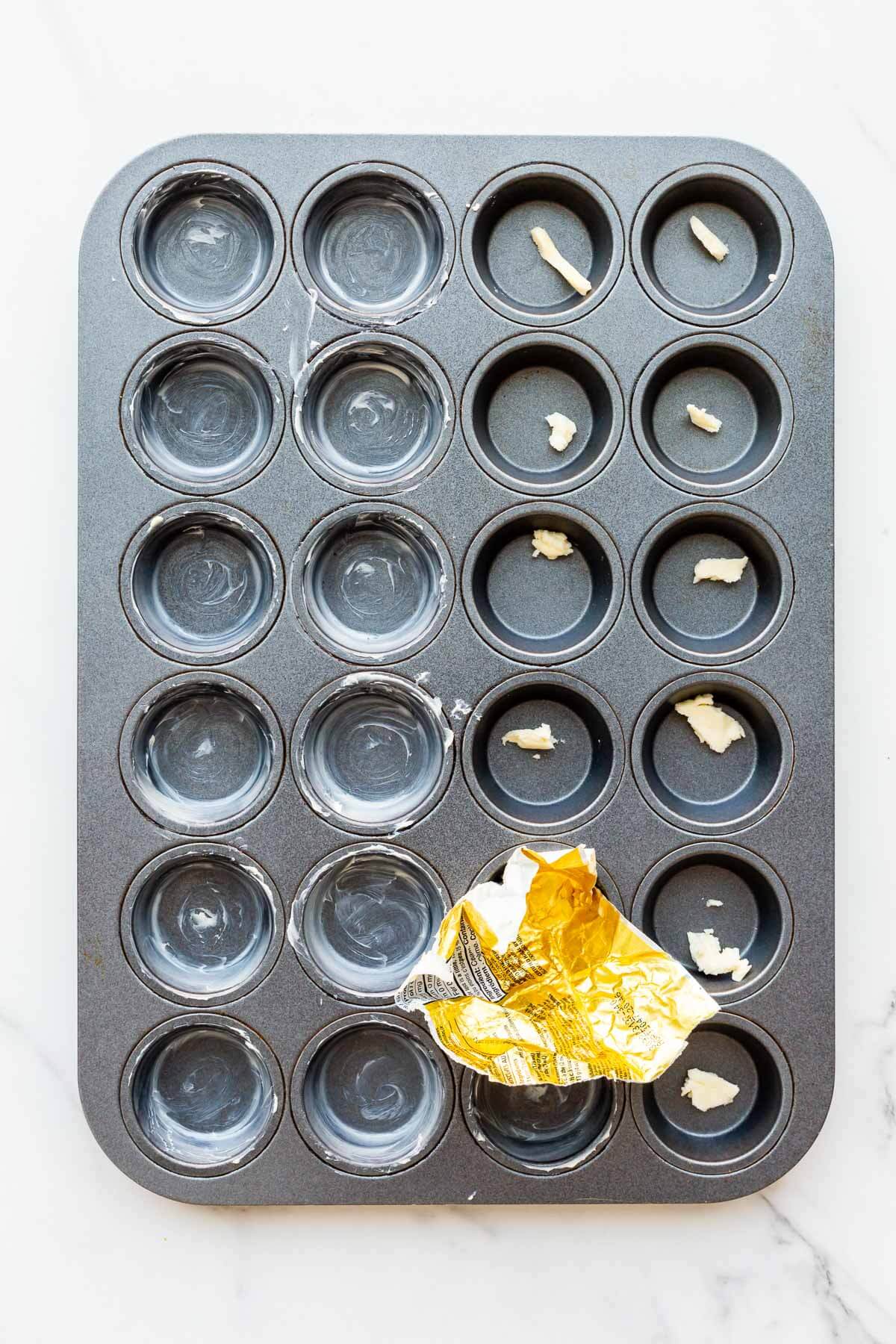 Buttering the wells of a mini muffin pan with softened butter and a butter wrapper.