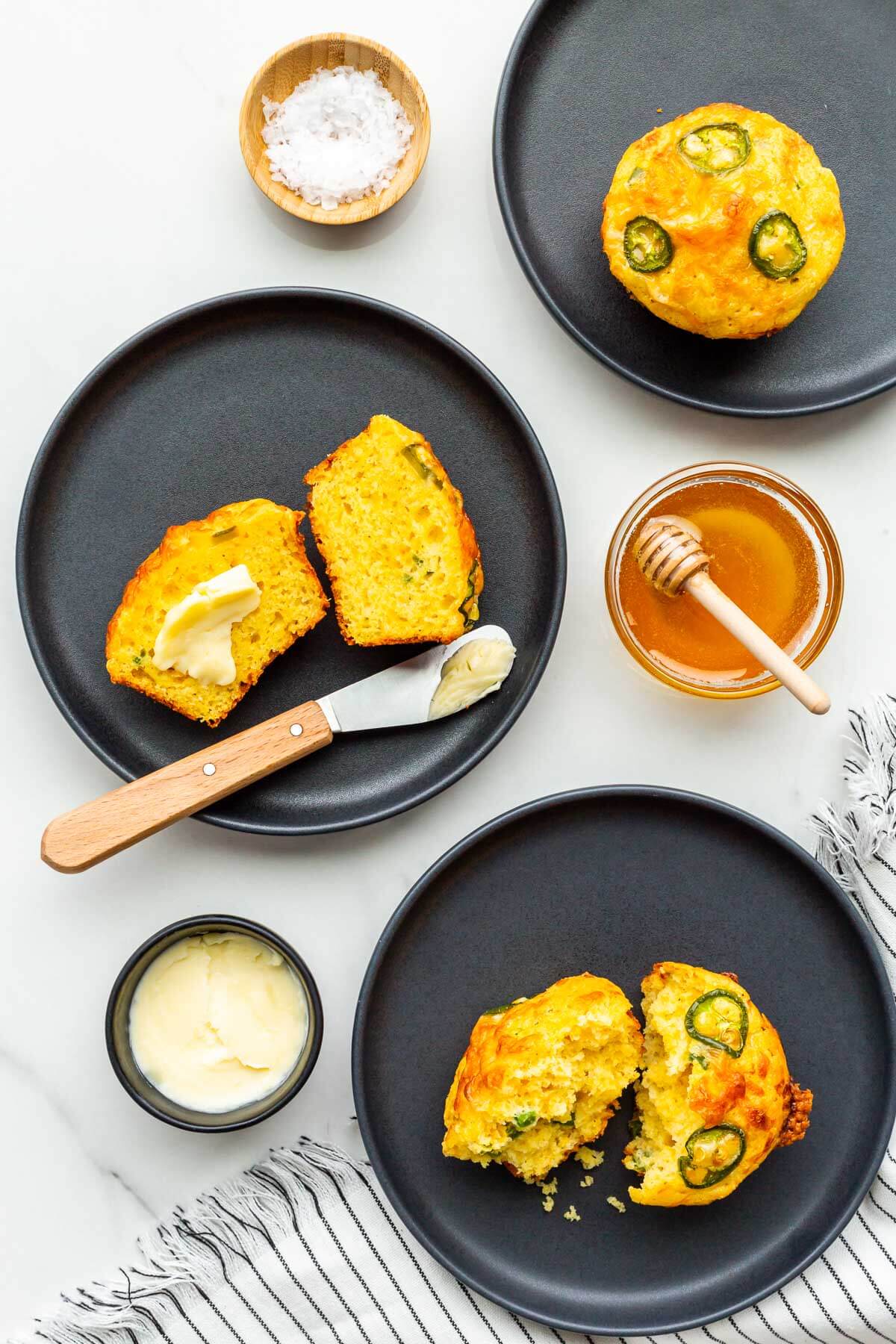 Cornbread muffins topped with cheese and jalapeño served on black plates.