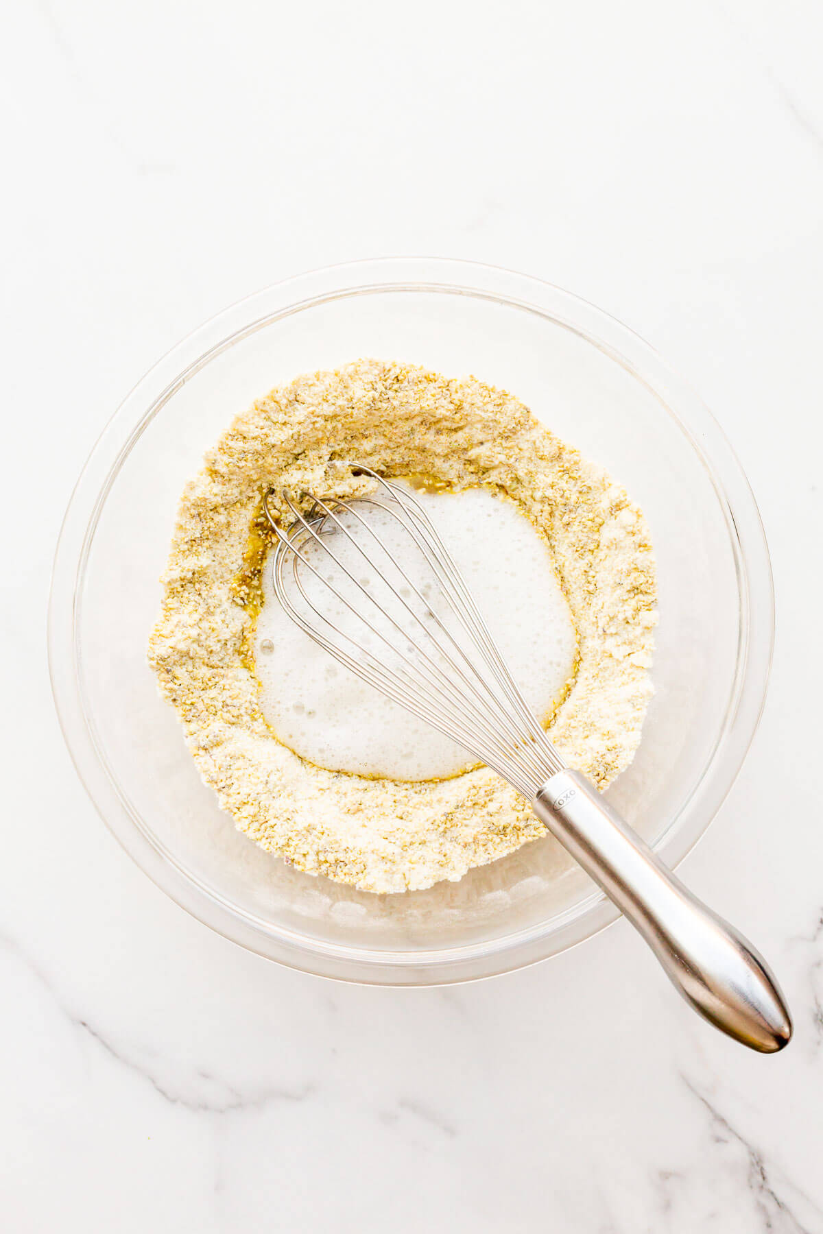 Whisking foamy egg whites into the dry mixture in a bowl to make pistachio financier cake batter.
