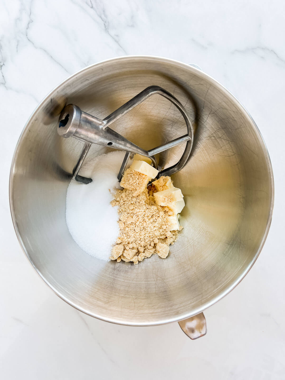 A mixer bowl with cubes of butter, two types of sugar (white and brown), and the paddle attachment.