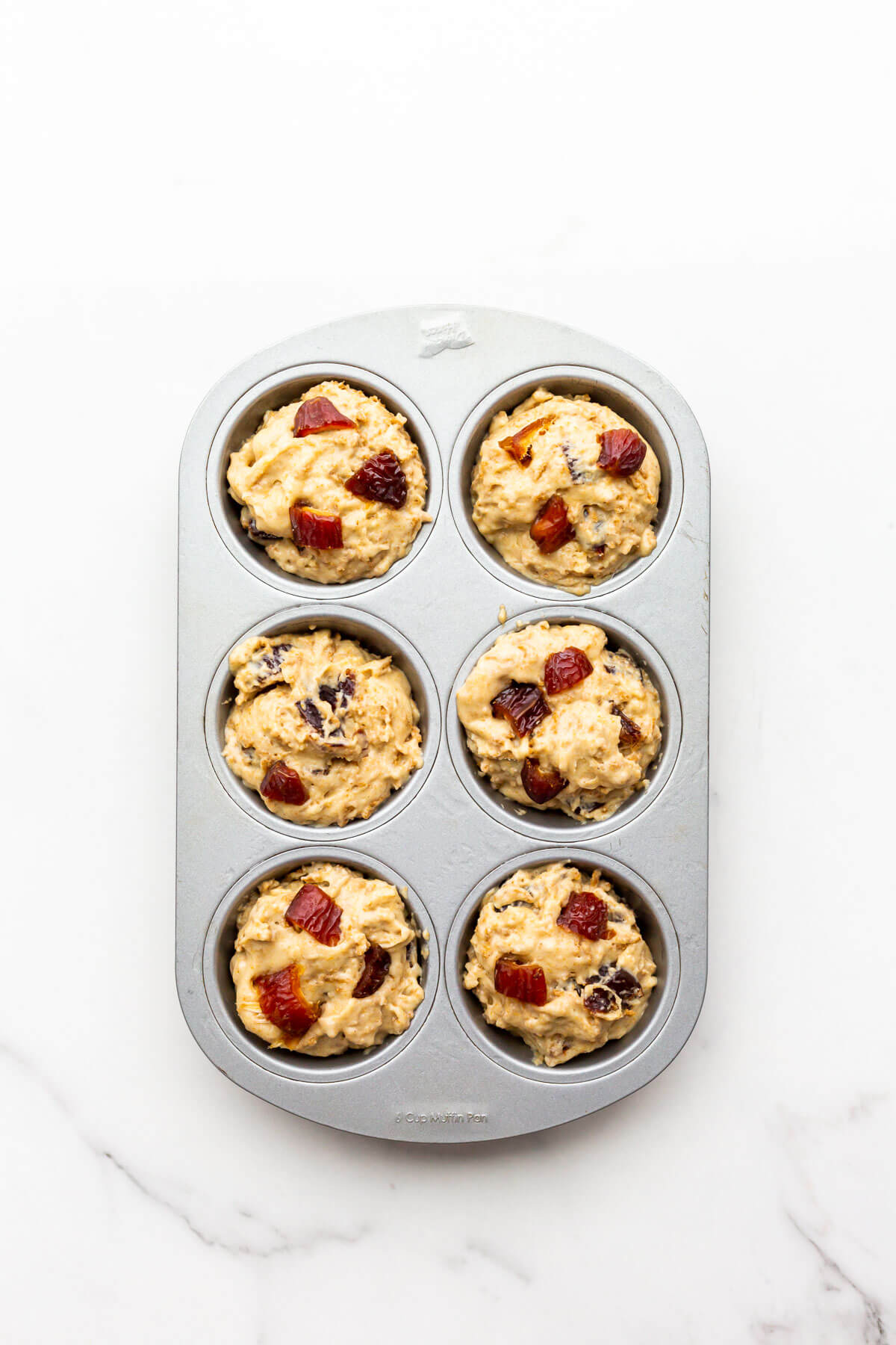 A six cup muffin pan of date bran muffins before baking in the oven.