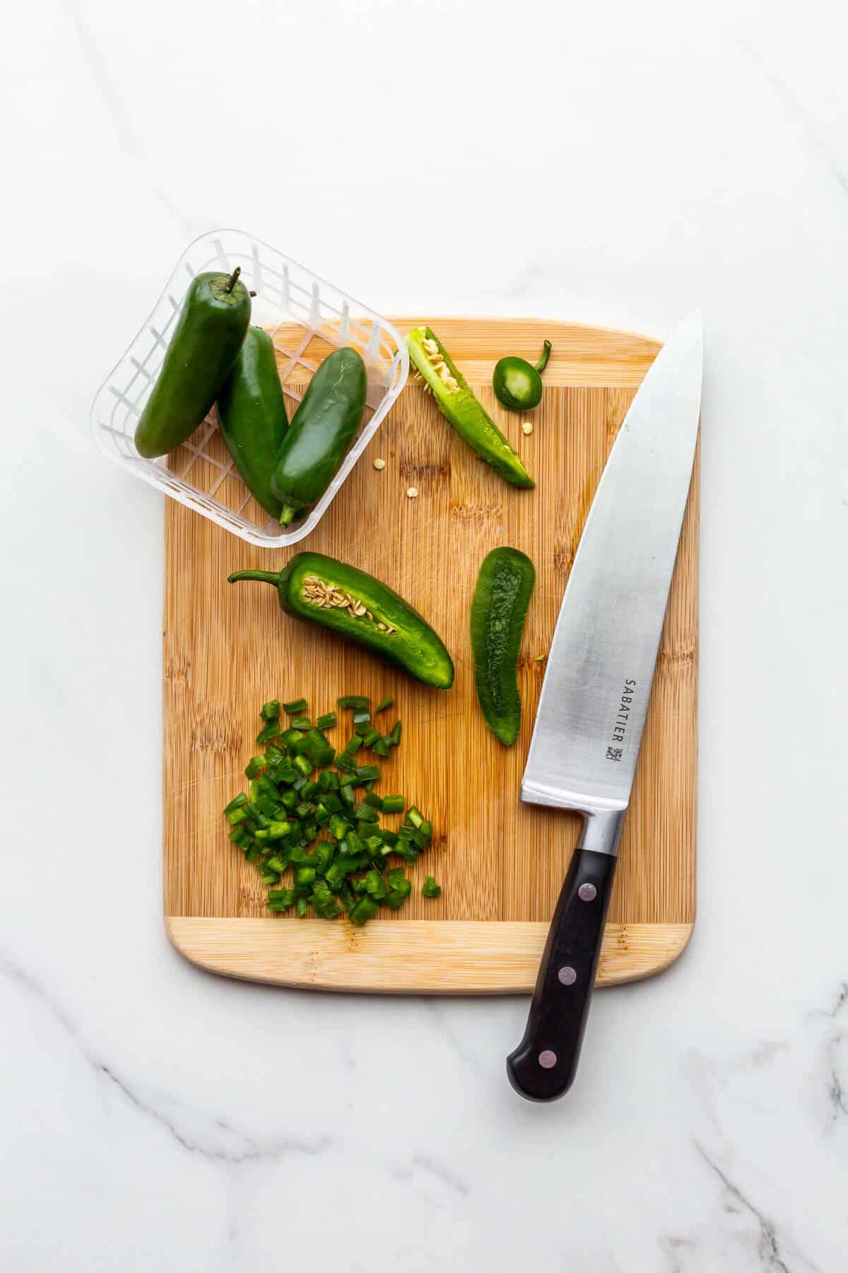 Dicing fresh jalapeño peppers on a wooden cutting board.