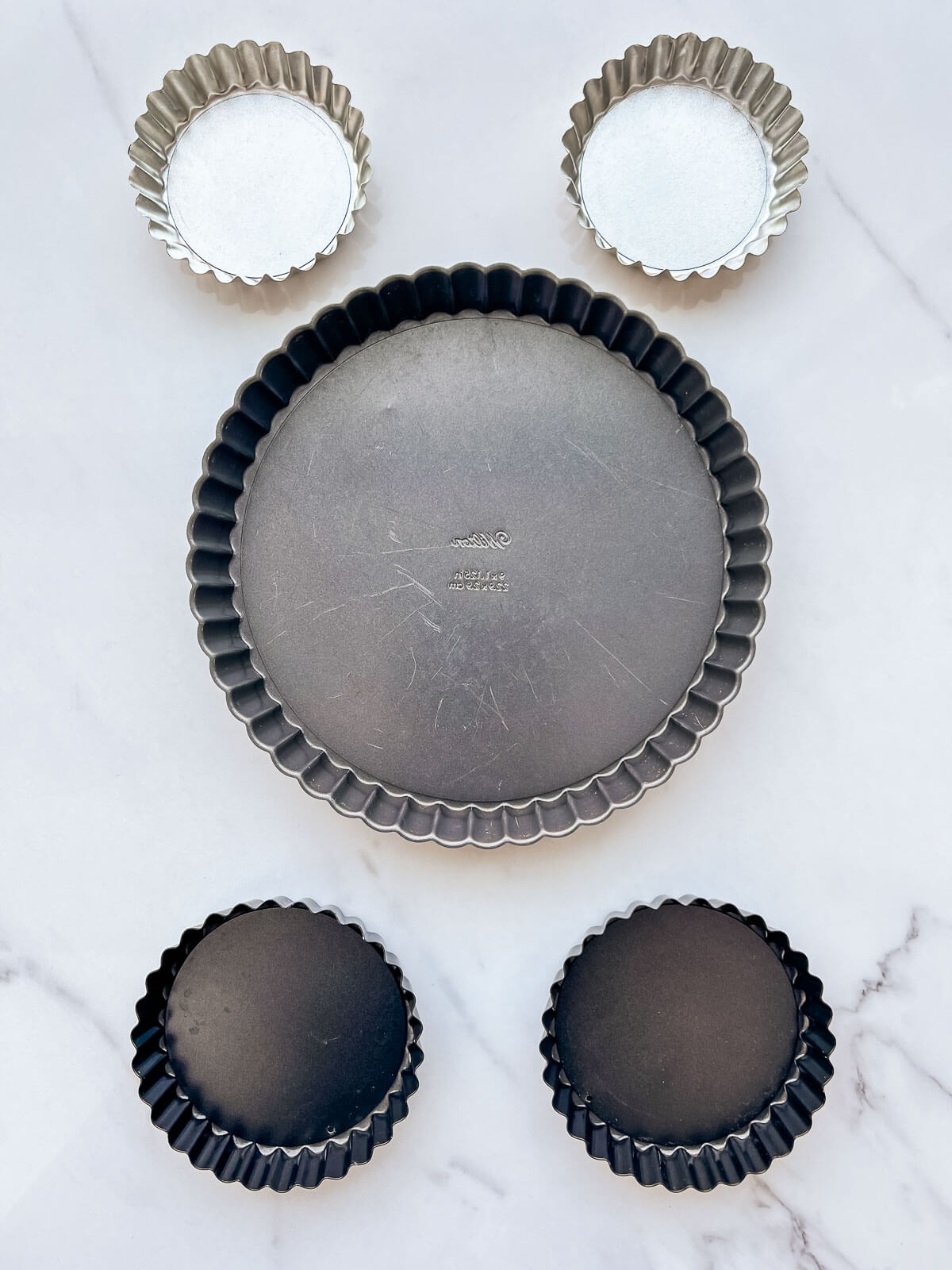 Tart pans of different sizes: two 4-inch mini tart pans, one 9-inch full-size tart pan, and two 4.5 inch mini tart pans.