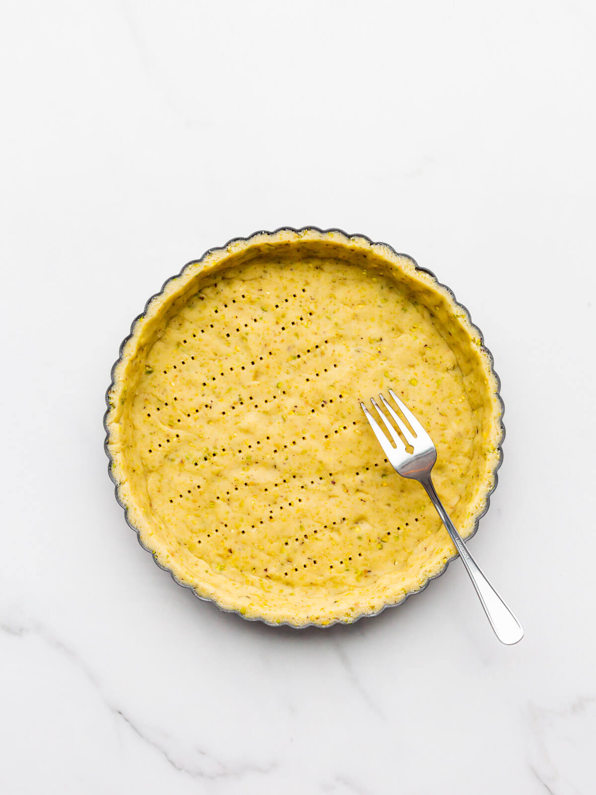 Poking holes with a fork into an unbaked tart shell to release steam as it bakes in the oven.