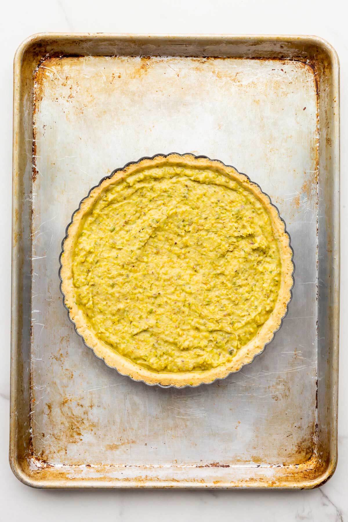 Unbaked pistachio tart in a fluted tart shell on a sheet pan ready for the oven.