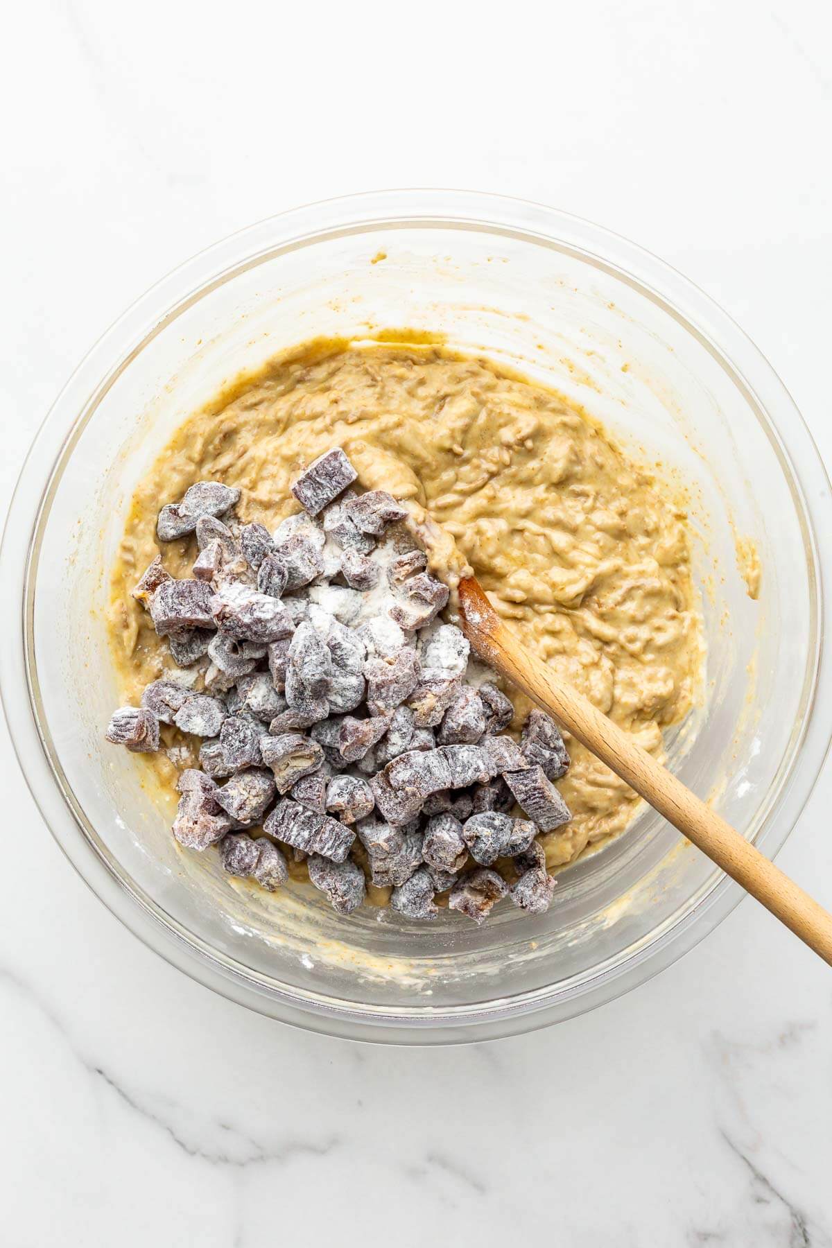 Folding chopped dates coated in flour into muffin batter in a glass bowl to make date bran muffins.