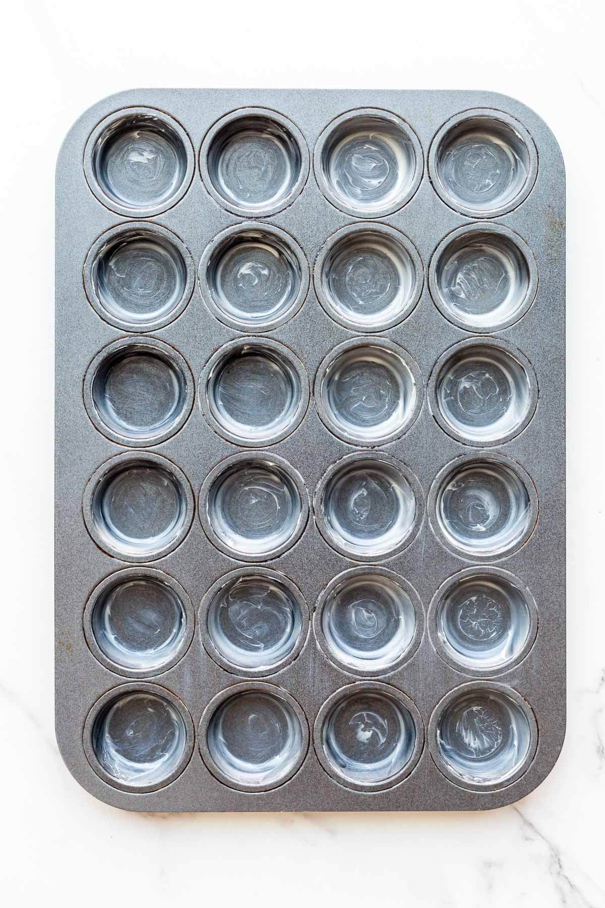 A greased mini muffin pan. The wells were greased with softened butter to coat the bottom and sides.