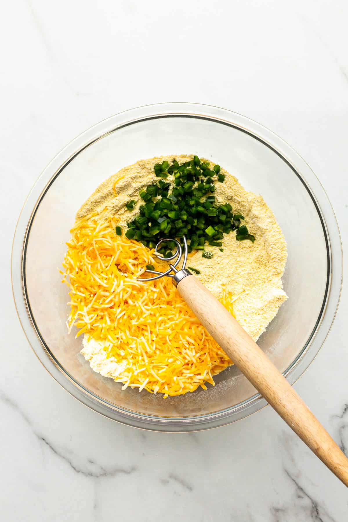 Whisking shredded cheese and diced jalapeño pepper into dry ingredients for cornbread.