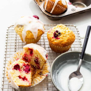 Drizzling lemon cranberry muffins on a wire rack with lemon icing.