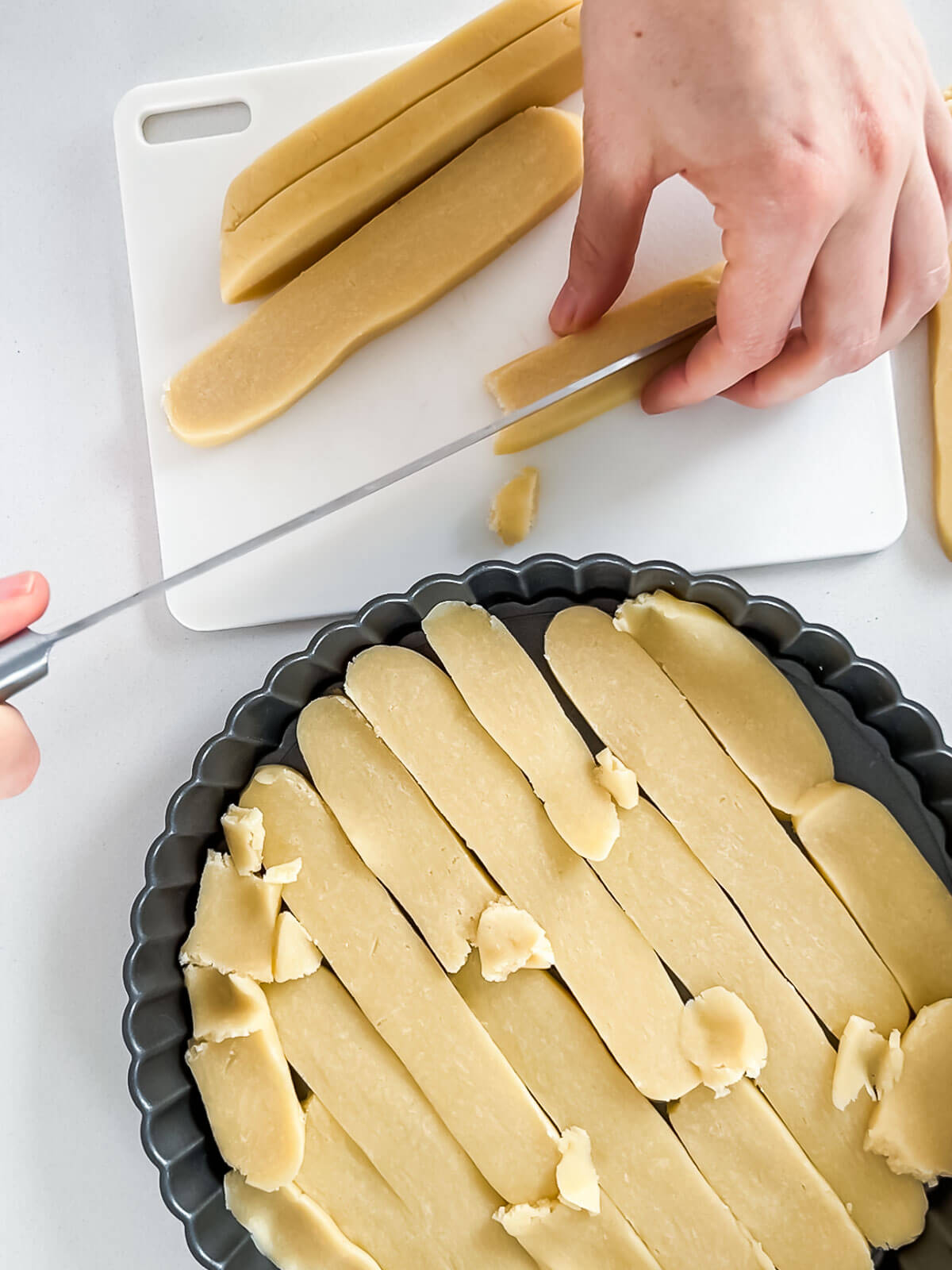 Slicing chilled tart dough in strips and laying them down to cover the surface and sides of a tart pan with an even layer, making the task easier.