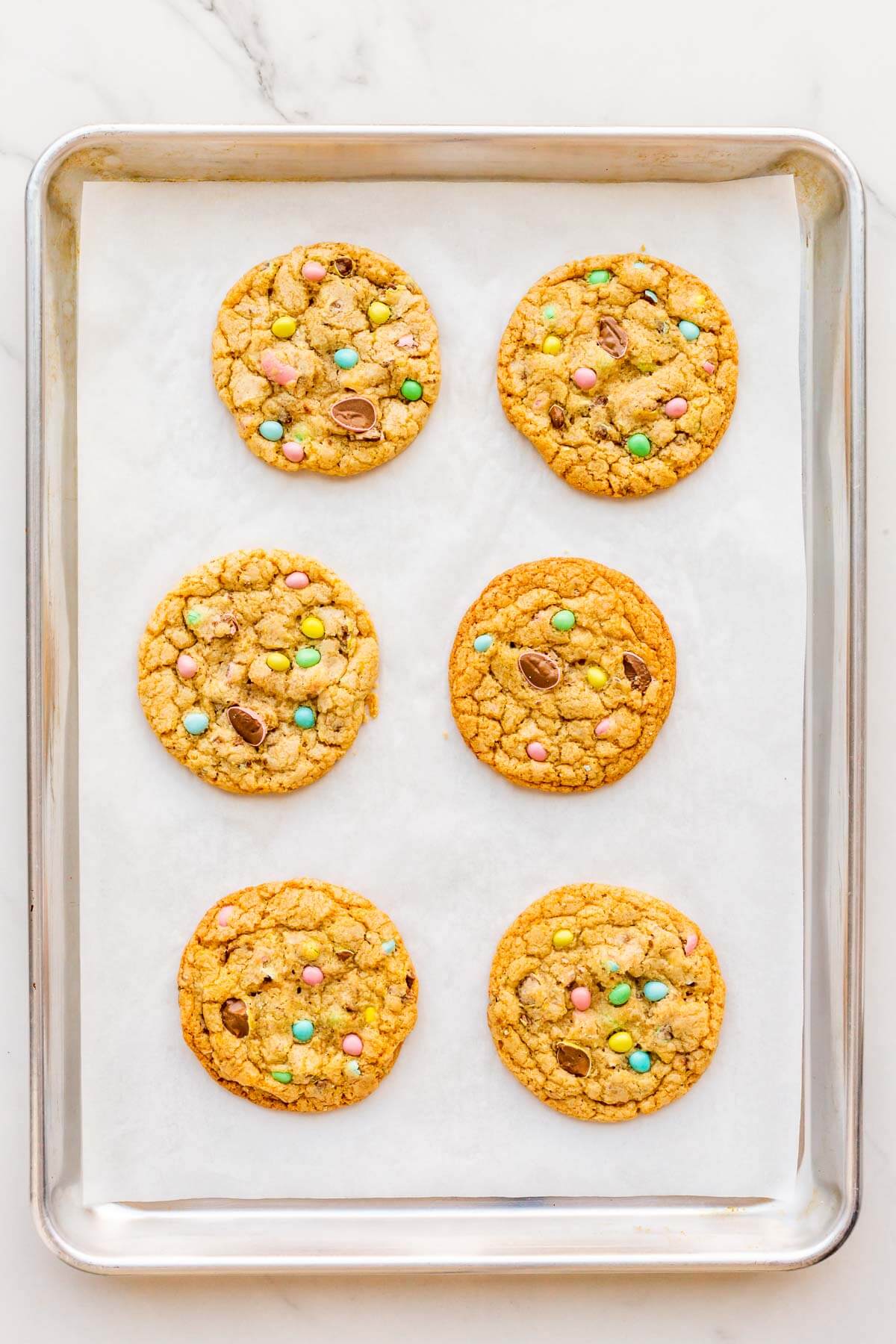 A parchment-lined sheet pan with 6 baked cookies topped with Mini Eggs.