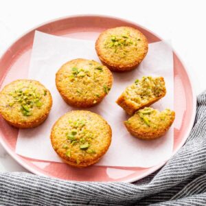 A pink plate with pistachio financiers, one of them broken open to show the crumb.