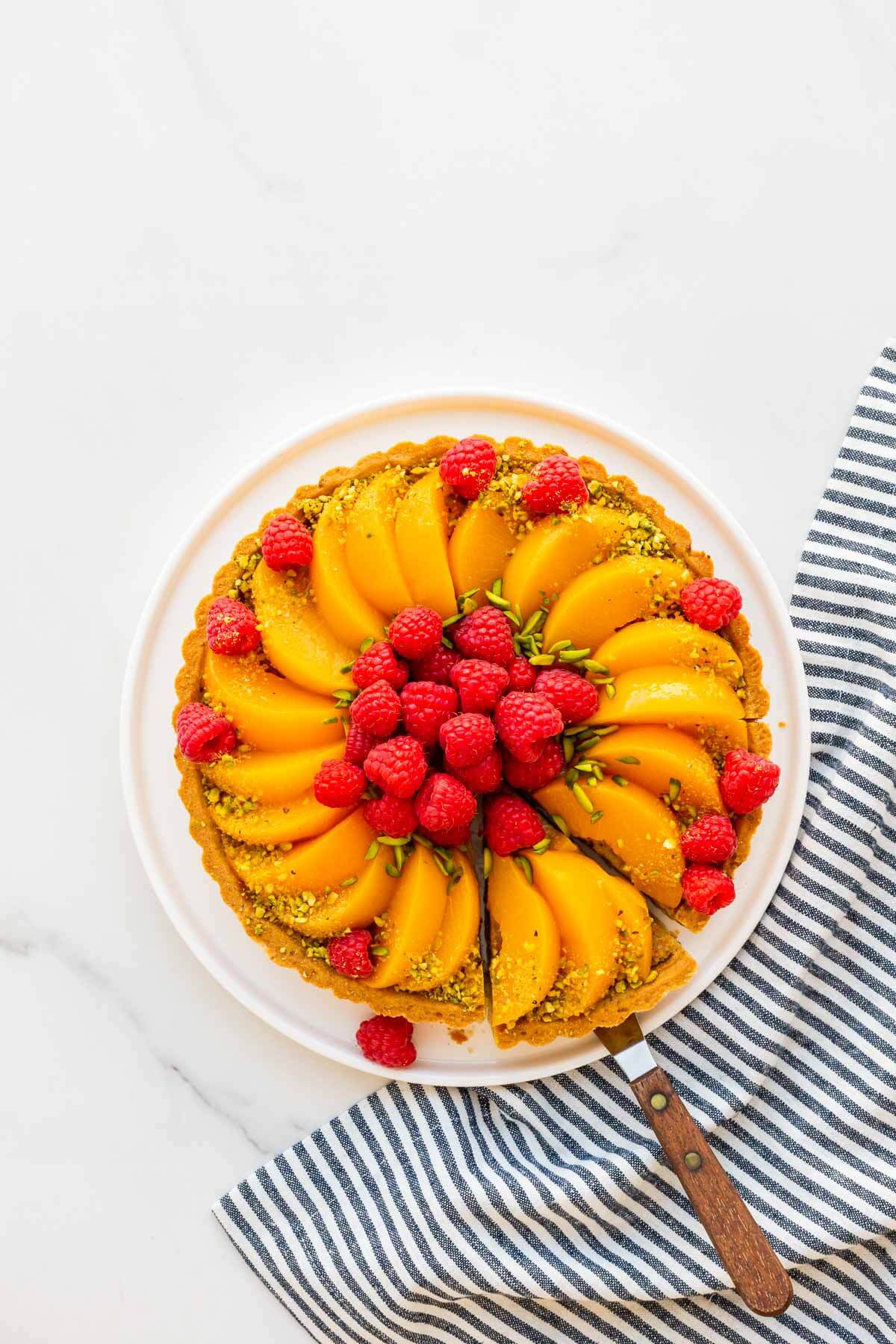 Slicing a pistachio tart topped with raspberries and peaches.