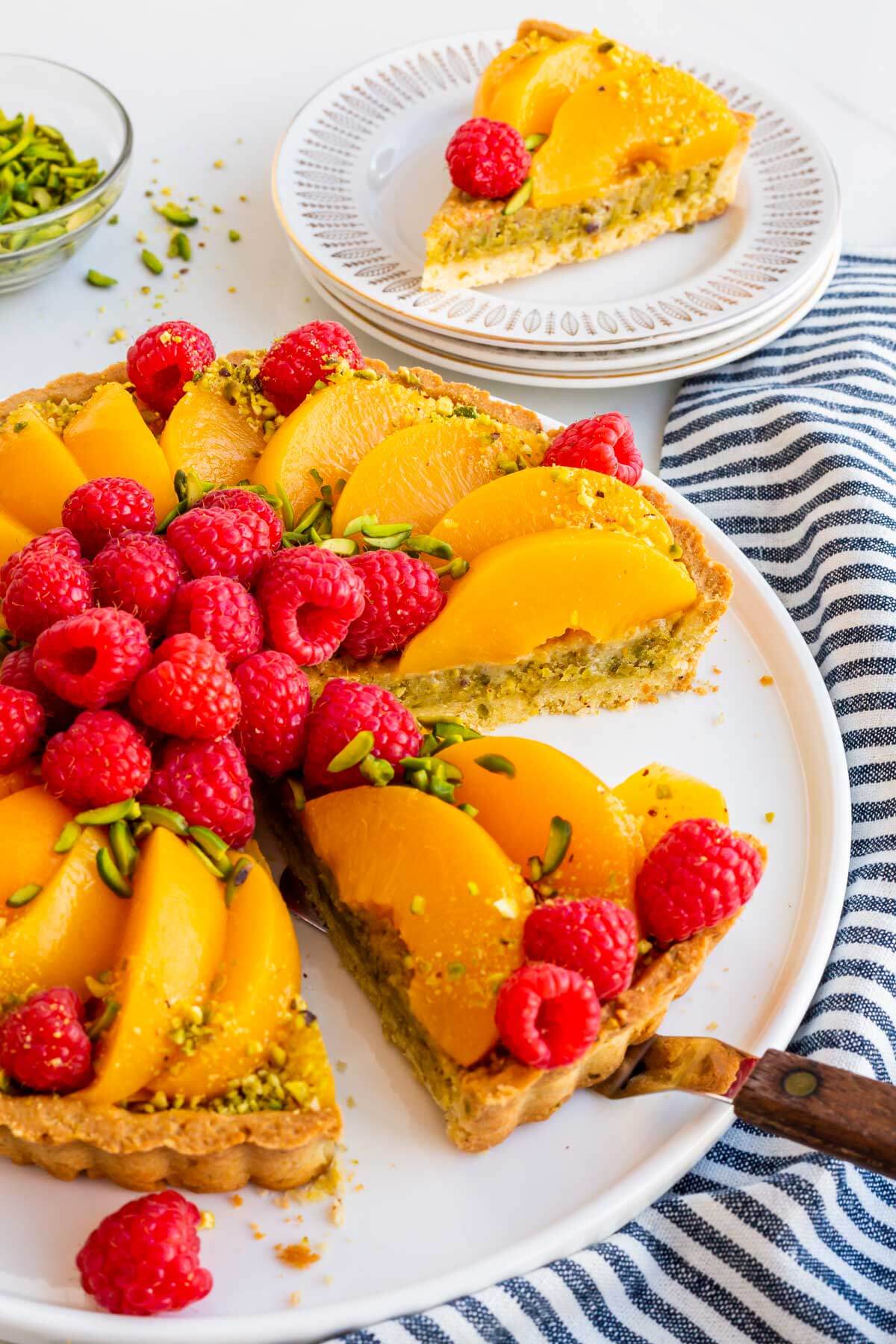 Serving a pistachio tart topped with raspberries and peaches.