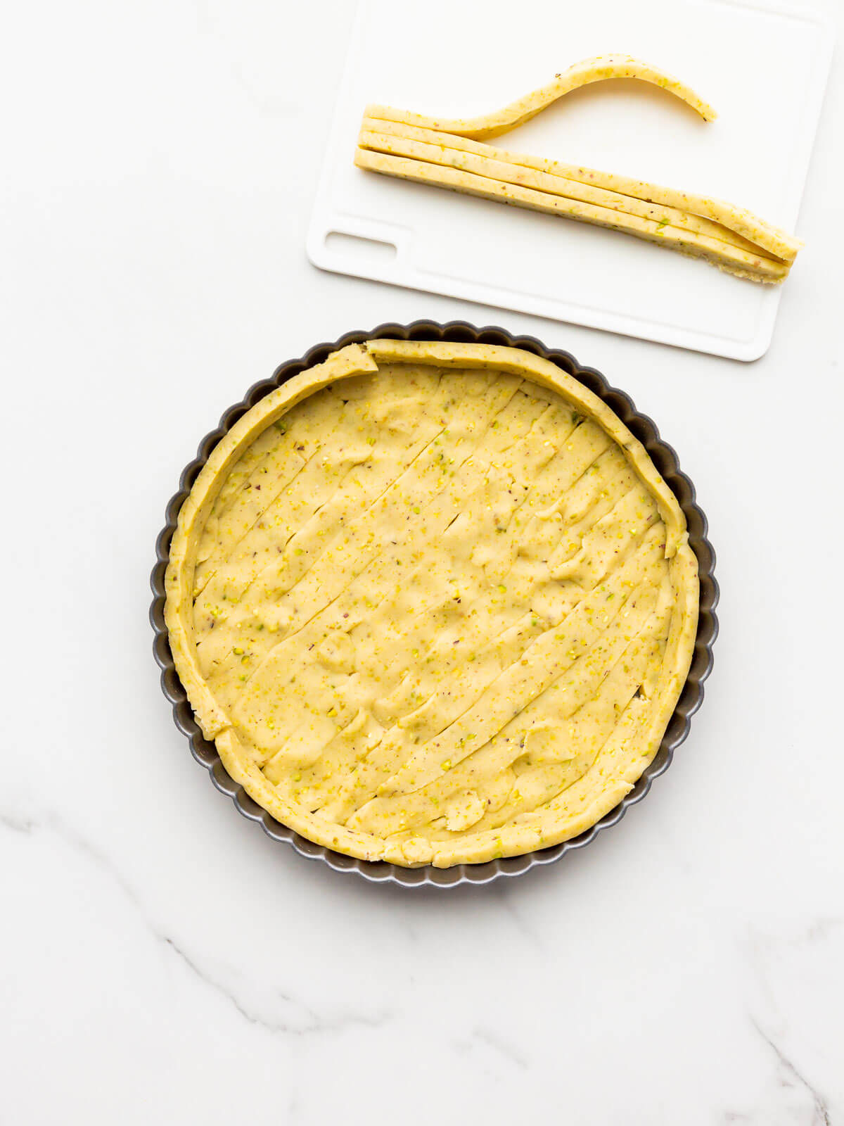 Lining tart pan with thin slices of unbaked sweet dough to make a pistachio tart shell.