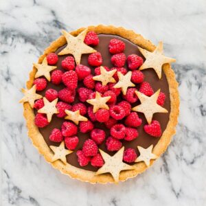 A raspberry chocolate tart garnished with star-shaped cookies and fresh rapberries.