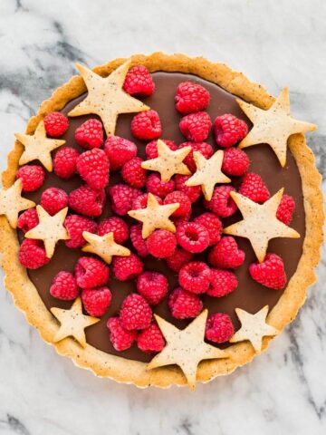 A raspberry chocolate tart garnished with star-shaped cookies and fresh rapberries.