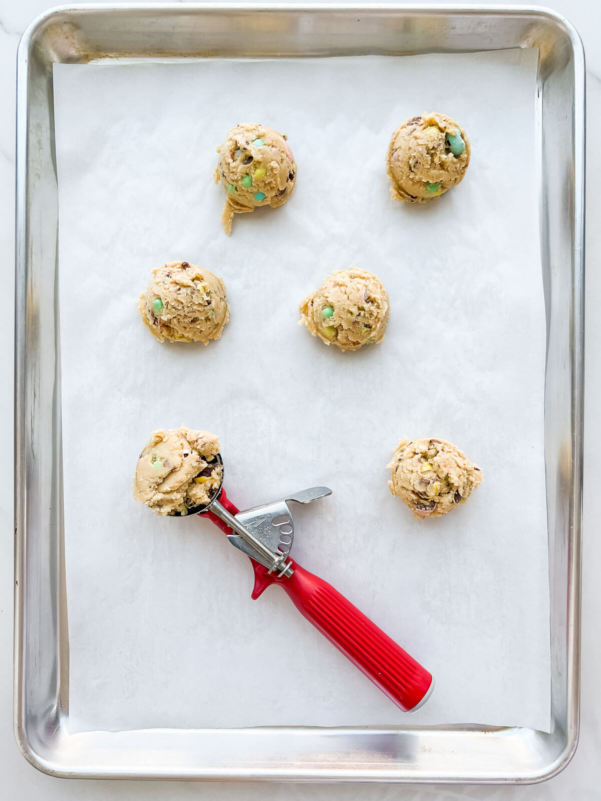 Scooping Easter cookie dough onto a parchment-lined sheet pan with a red-handled cookie scoop.