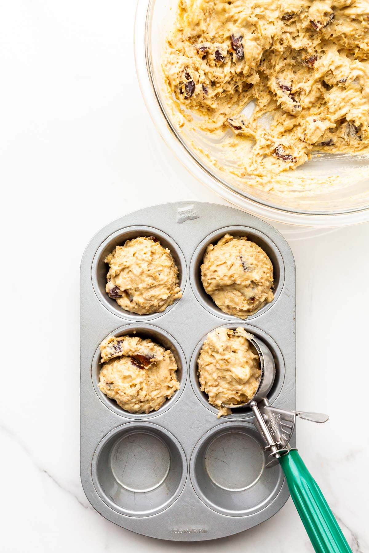 Dividing bran muffin batter between the cups of a muffin pan using a scoop.