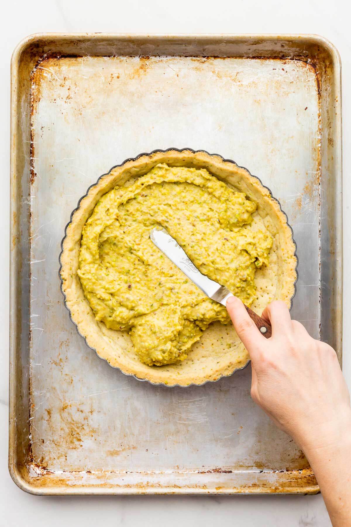 Spreading a pistachio cream filling over a baked pistachio crust with an offset spatula to make a tart.