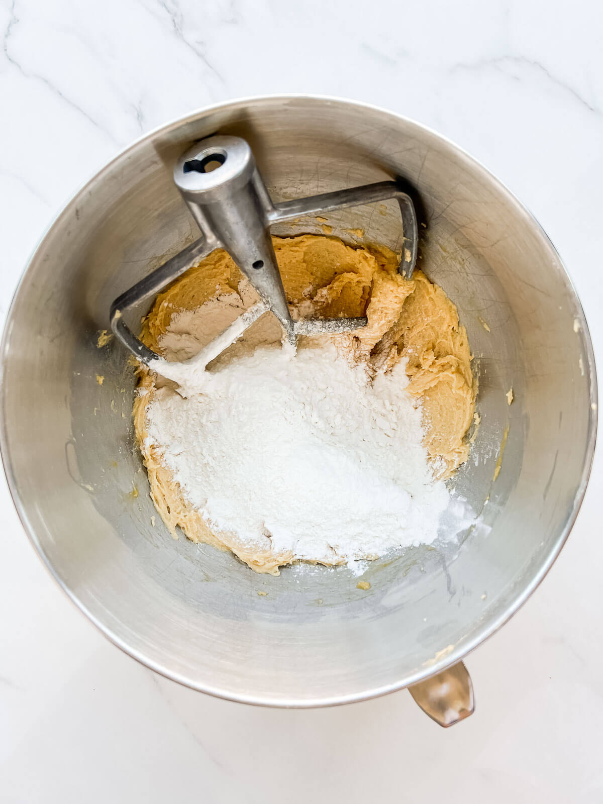 Adding flour to a mixer bowl of cookie dough to make Easter cookies with Mini Eggs.