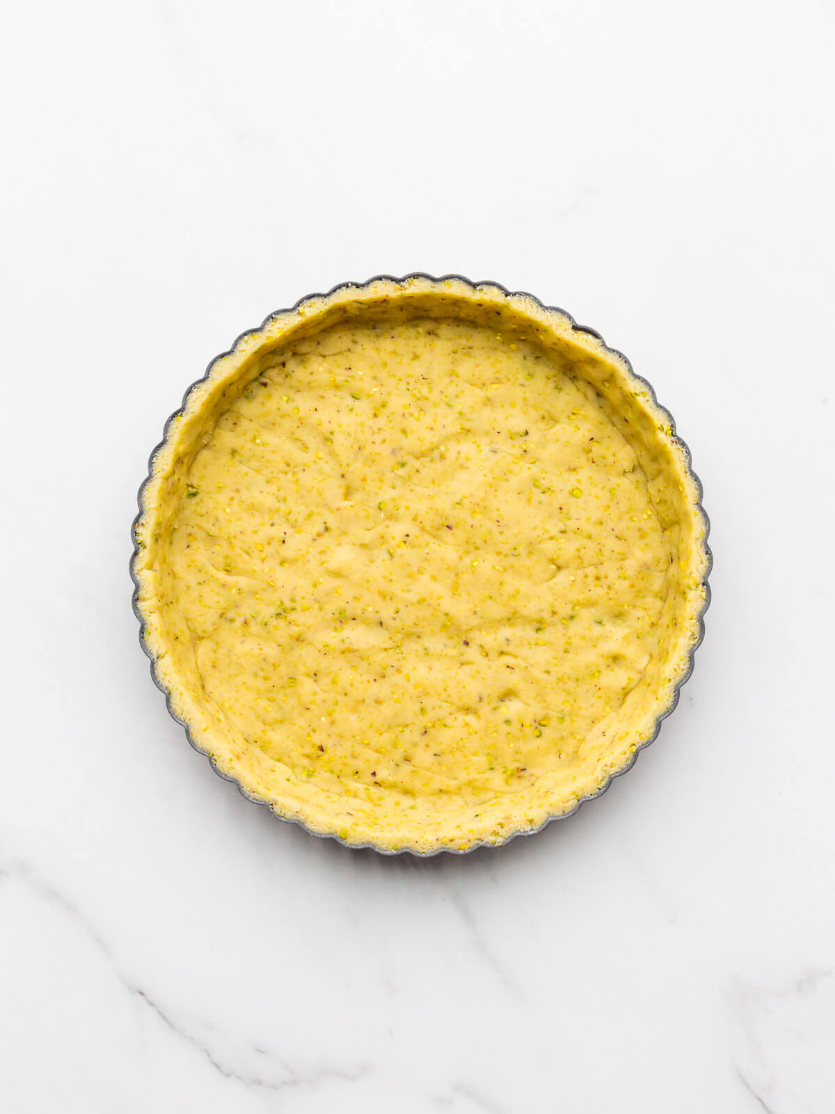 Trimmed unbaked pistachio tart shell in a fluted tart shell.