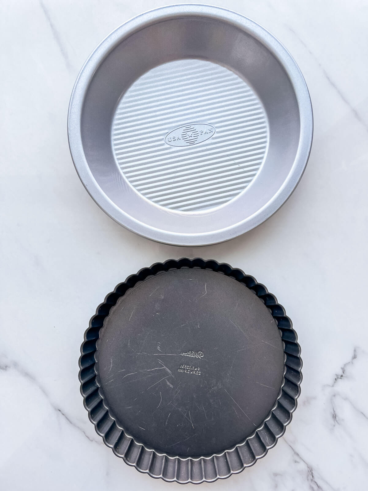 A metal pie plate next to a tart pan with a fluted edge to show the difference in shape.