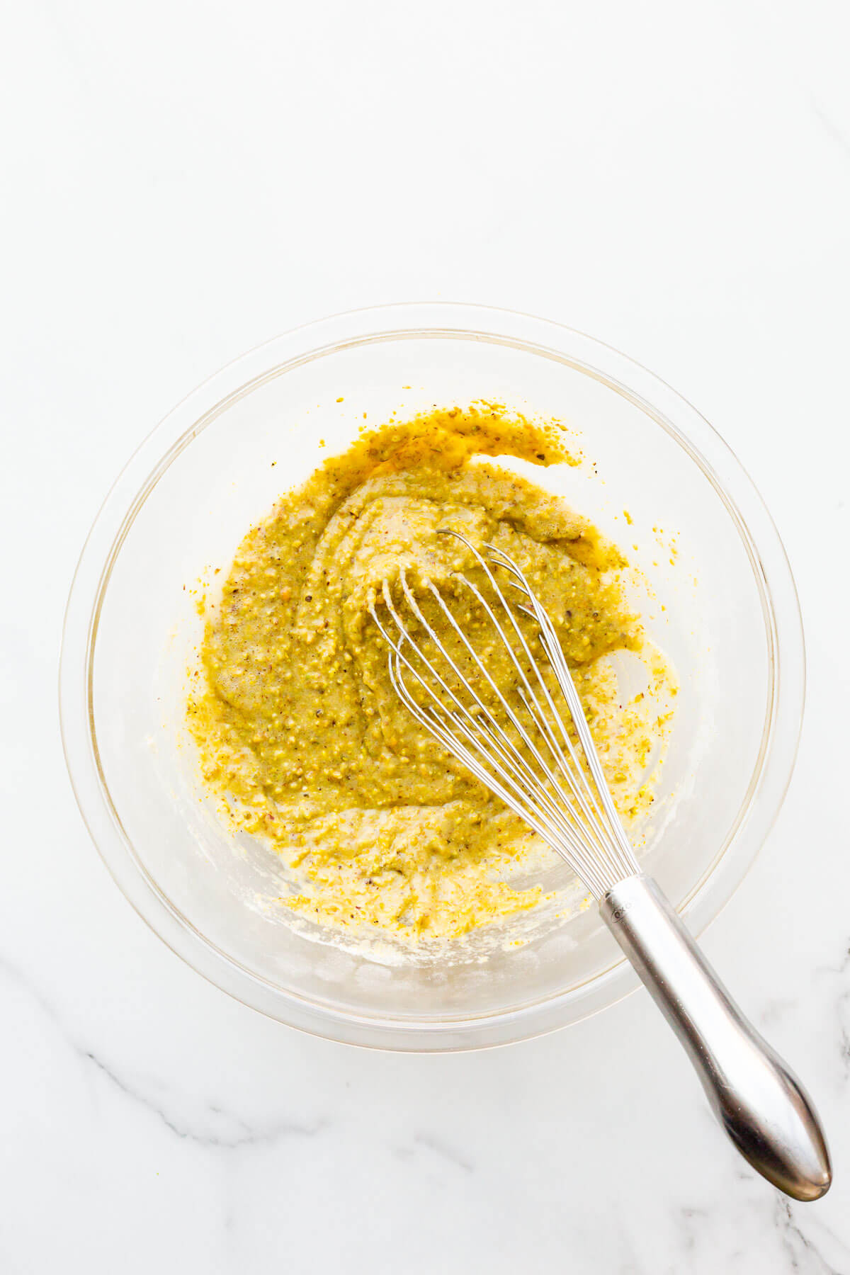 Thick pistachio financier batter in a glass bowl with a whisk.