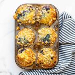 A pan of baked honey blueberry muffins with streusel topping.