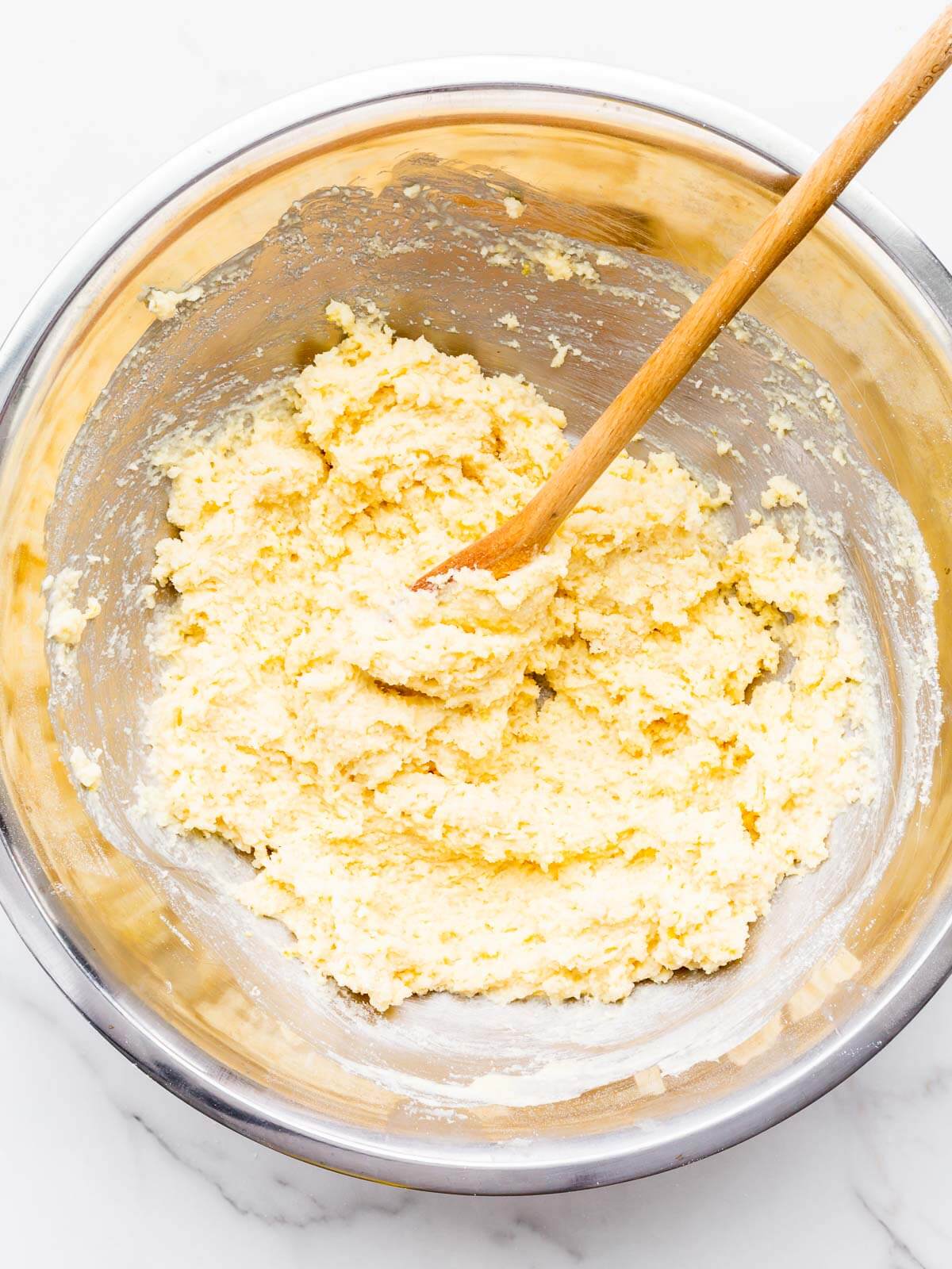 A very thick lemon muffin batter in a stainless steel mixing bowl.