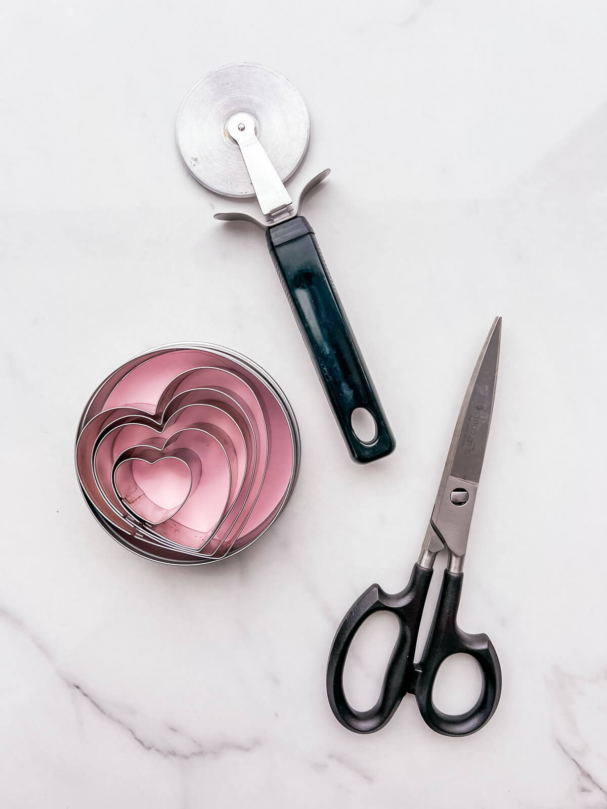 Tools that are useful to cut pie dough to make pie, including kitchen scissors, a pizza wheel cutter, and cookie cutters.