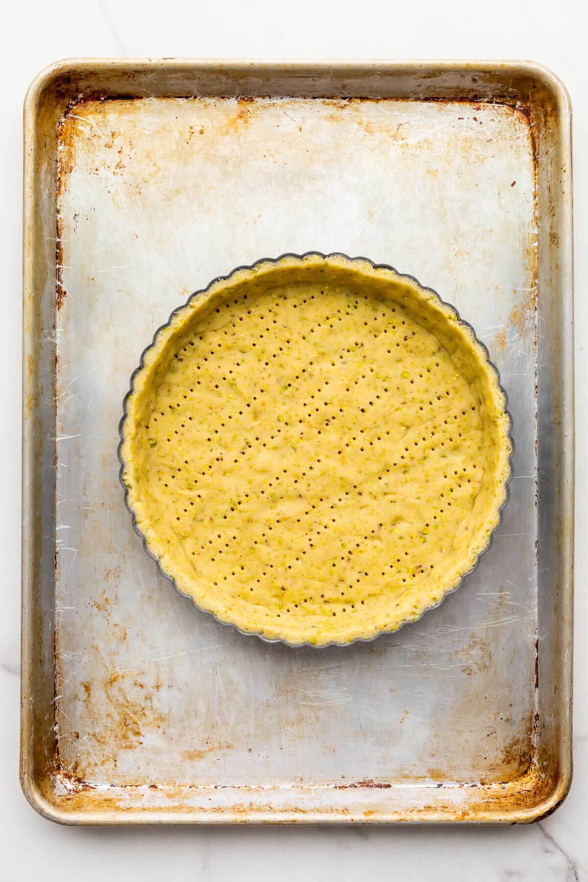 Docked pistachio tart shell before baking on a sheet pan.