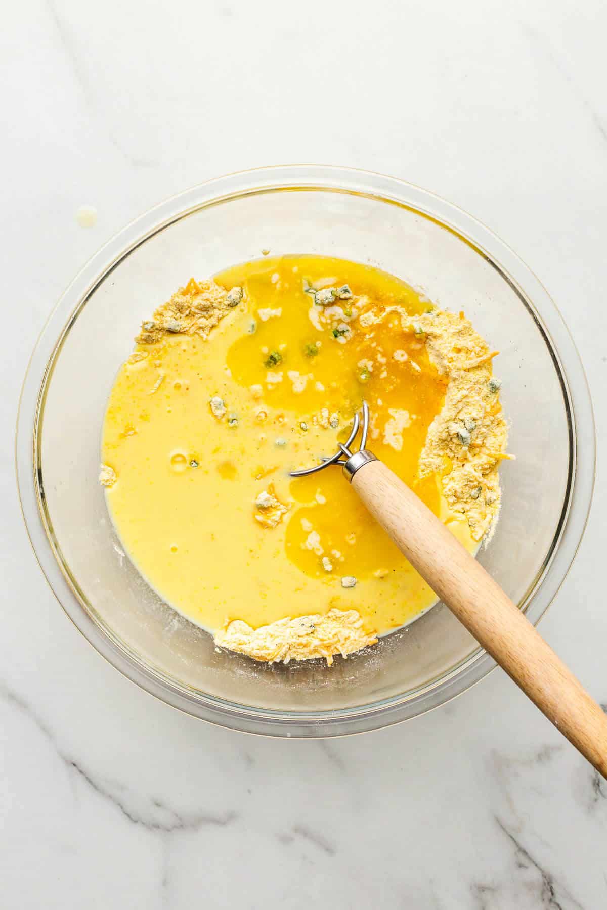 Combining wet and dry ingredients together in a large glass bowl to make cornbread muffins.