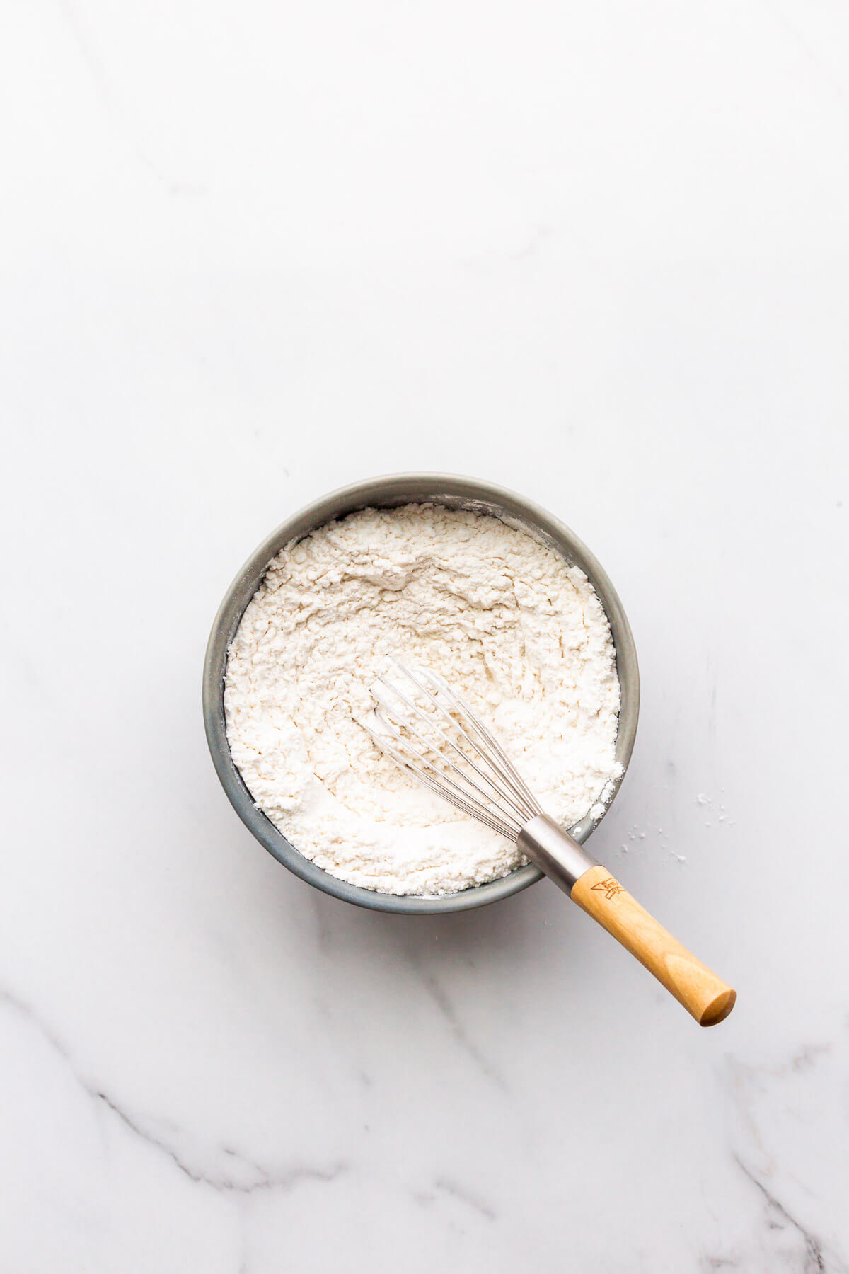 Whisking dry ingredients in a ceramic bowl with a small whisk, including flour, baking soda, and salt.