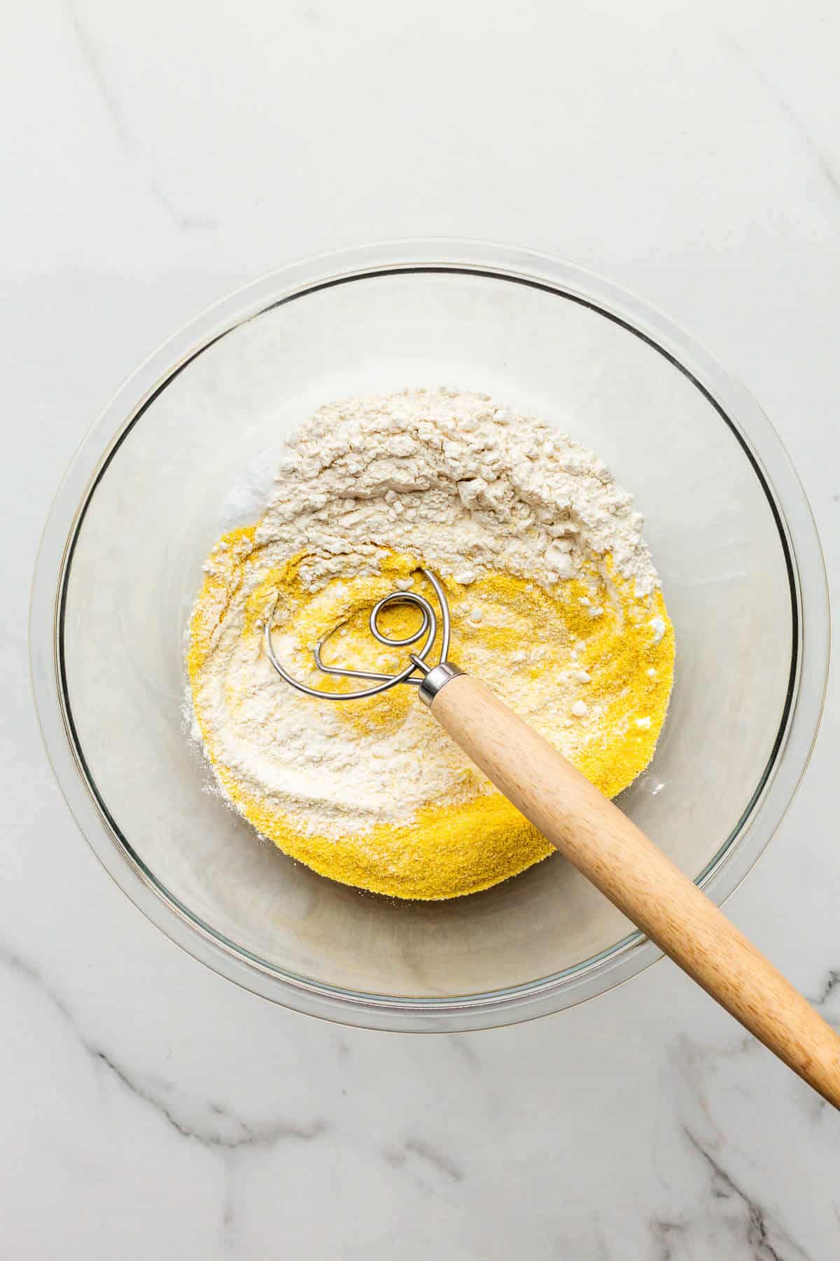 Whisking dry ingredients together in a glass bowl to make cornbread.