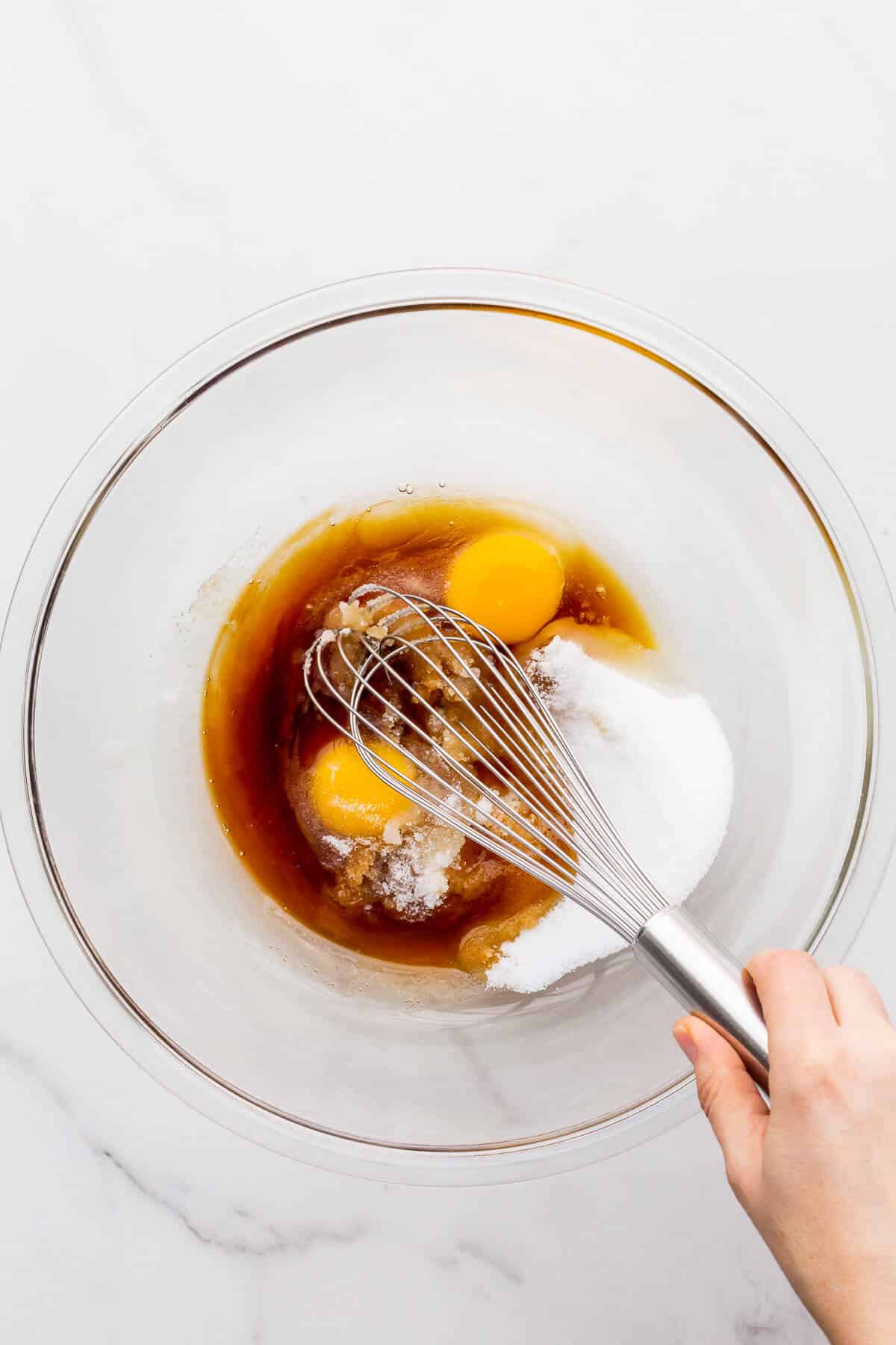 Whisking the wet ingredients to make muffins, including eggs, sugar, maple syrup, and vanilla.