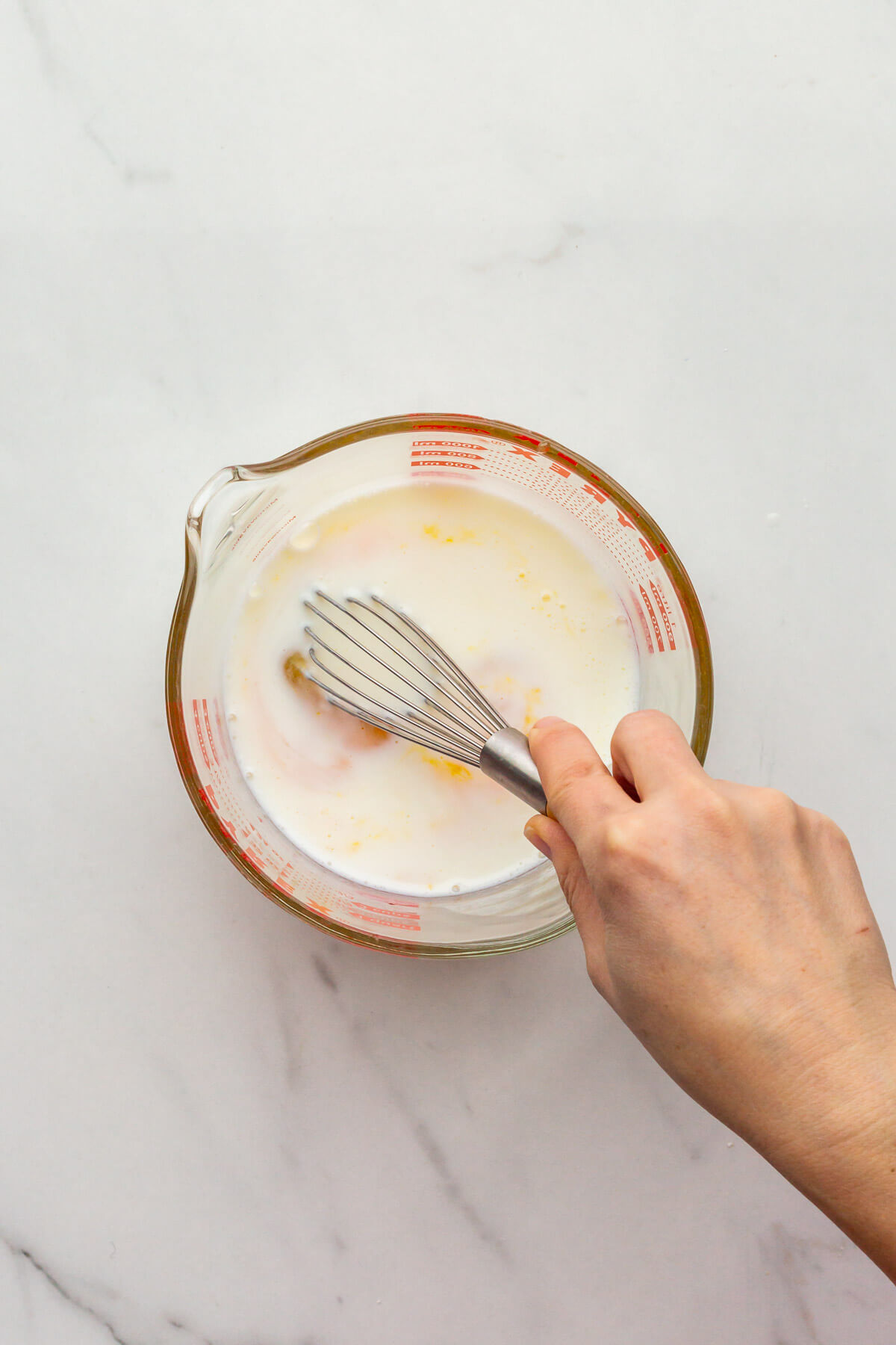 Whisking wet ingredients, including eggs and buttermilk, to make cornbread.