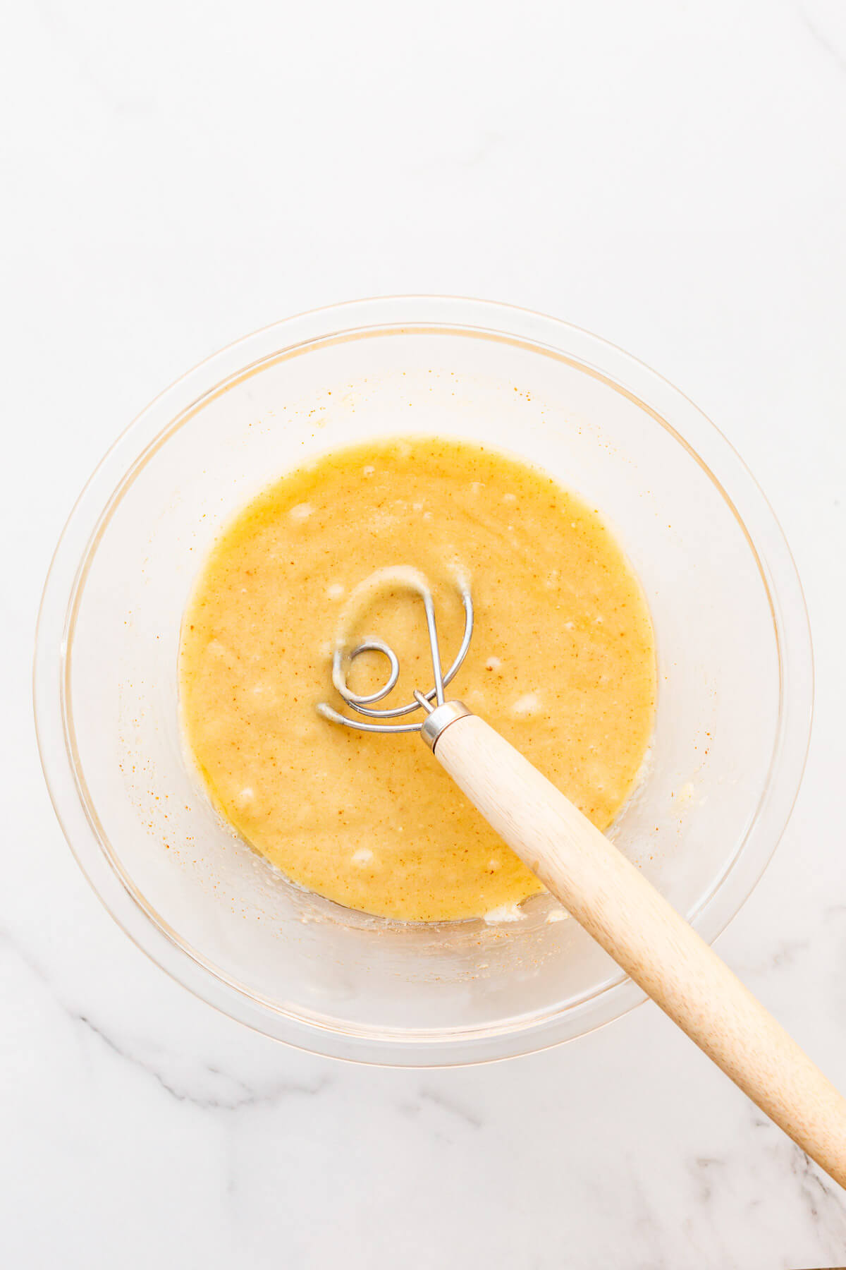 Almond financier batter in a glass bowl after mixing in brown butter.