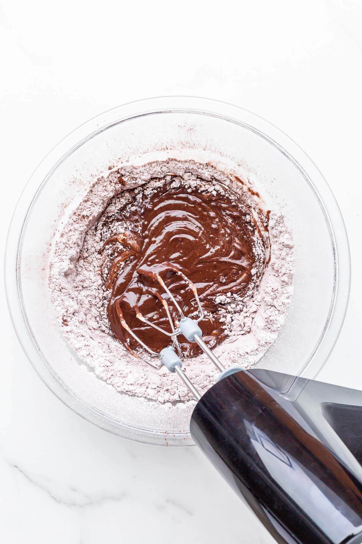 Beating ingredients in a glass bowl with an electric mixer to make chocolate fudge frosting.