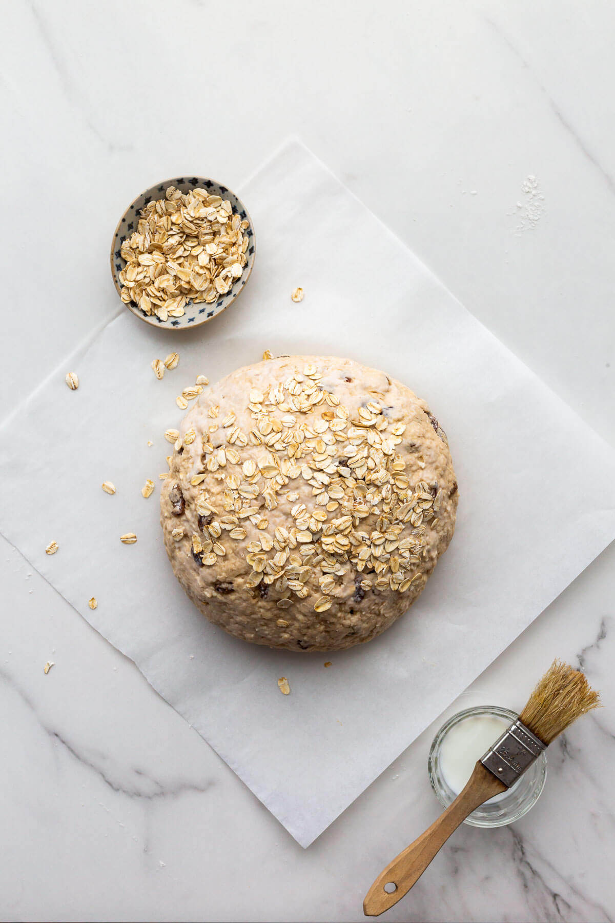 Brushing soda bread with buttermilk to help oats adhere to the surface of the bread before baking.