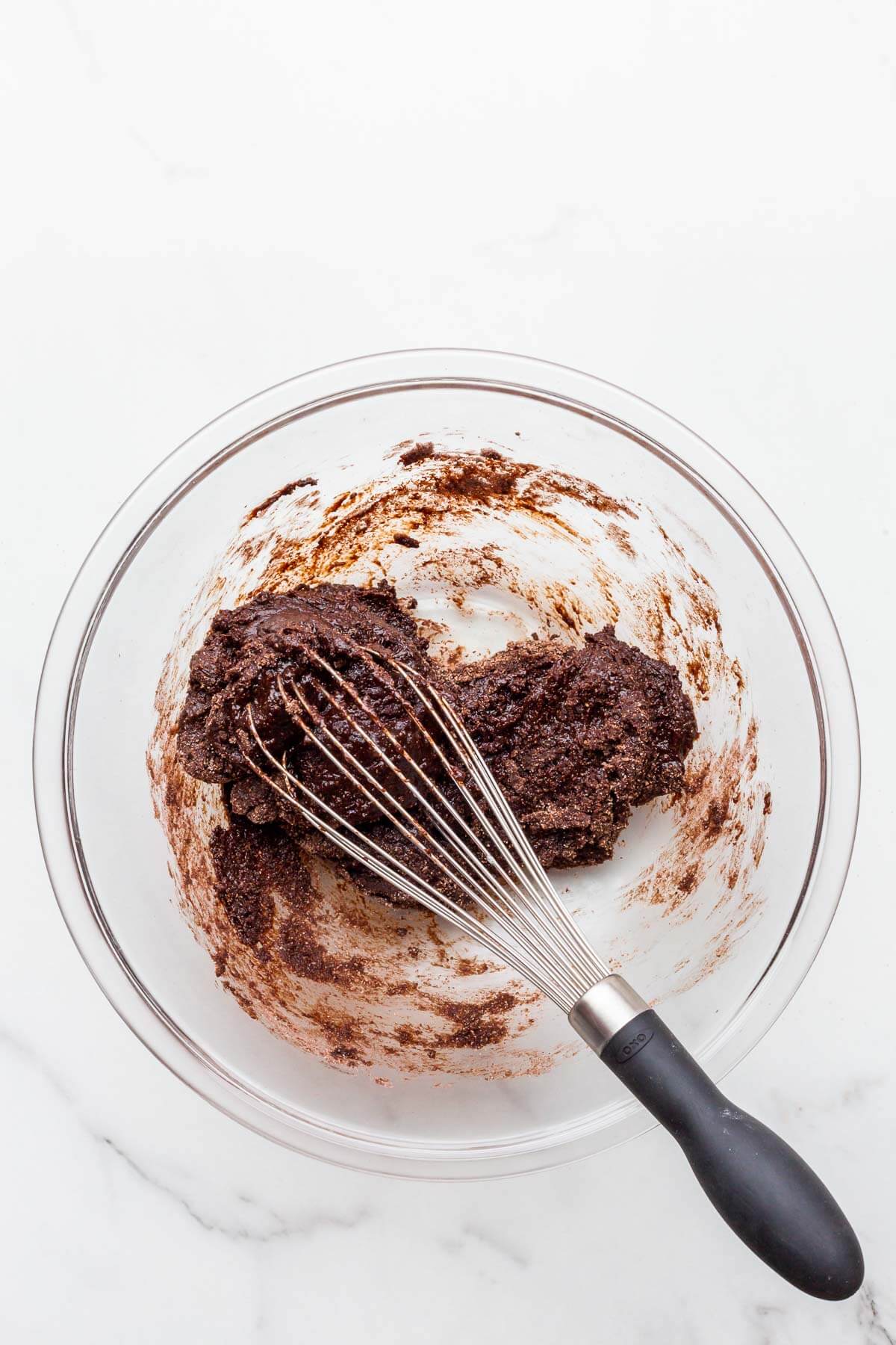 Thick chocolate cake batter in a glass bowl mixed with a whisk.