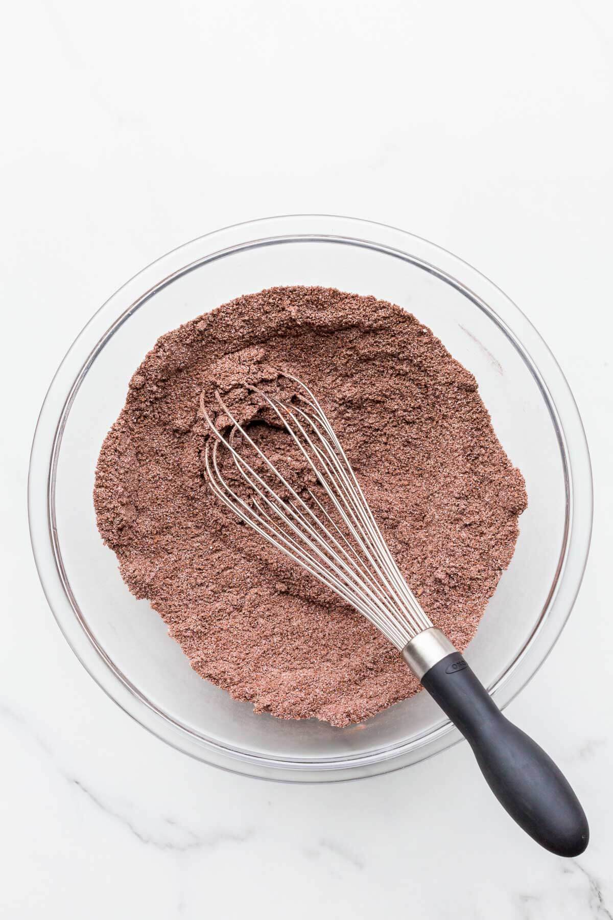 Dry ingredients to make chocolate financiers mixed in a glass bowl with a whisk.