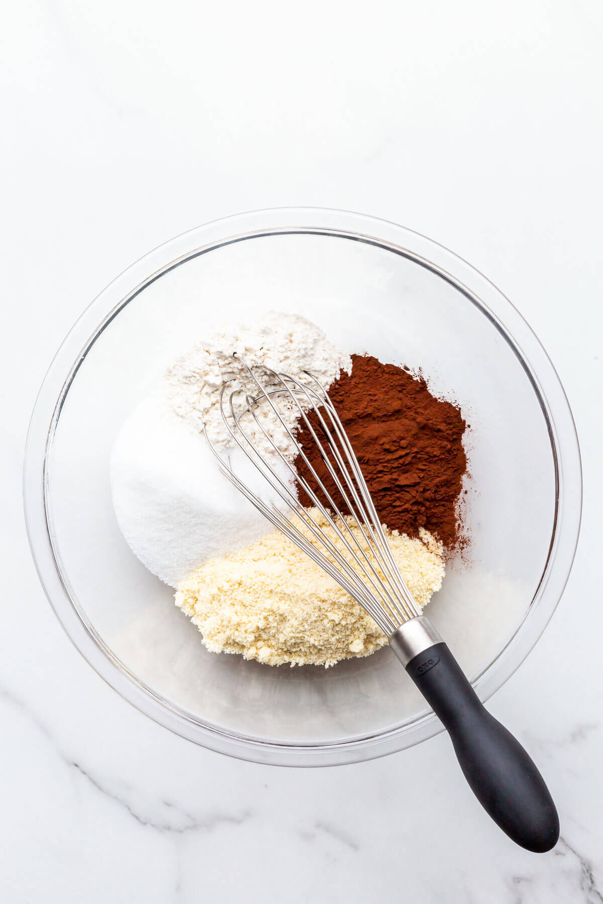 A glass bowl with dry ingredients to make financiers, including ground almonds, flour, sugar, and cocoa powder.