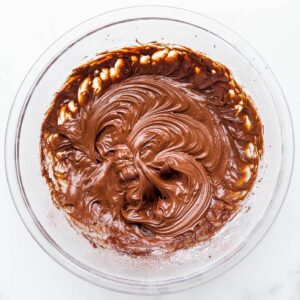 A glass bowl of glossy chocolate sour cream frosting.